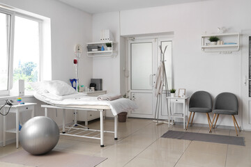 Interior of hospital ward with bed, door and chairs