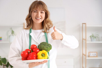 Female nutritionist with healthy vegetables showing thumb-up in office