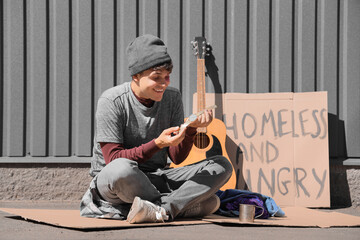 Young homeless man with wristwatch sitting on street