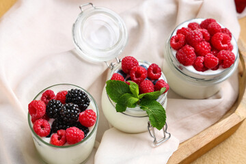Glass and jars of tasty yogurt with different fresh berries on table, closeup