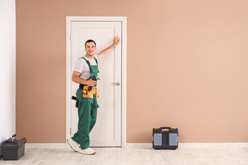 Male worker with electric drill near door at home