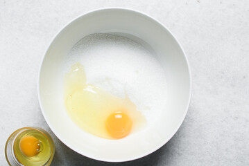 Overhead view of egg and sugar in a bowl on a marble countertop, process of making a cake
