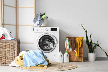 Interior of light bathroom with washing machine, pile of dirty clothes and laundry basket