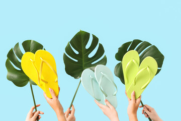 Female hands with flip-flops and monstera leaves on blue background. Travel concept