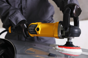 Man polishing car hood with orbital polisher indoors, closeup