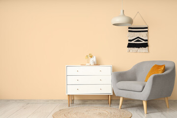 Interior of modern room with comfortable armchair and home decor on commode near beige wall