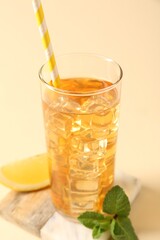 Fototapeta premium Refreshing iced tea with drinking straw in glass, mint and slice of lemon on beige background, closeup