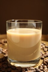 Coffee cream liqueur in glass and beans on tray, closeup