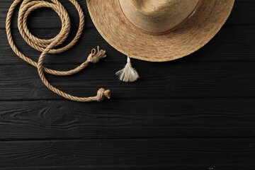 Cotton rope and straw hat on black wooden background, flat lay. Space for text