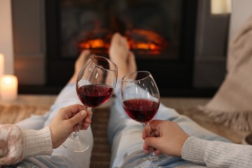 Couple with glasses of wine near fireplace on floor at home, selective focus