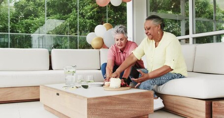 Senior friends celebrating 60th birthday in modern home space with wooden table and desserts