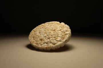 Minimalist photo of a single puffed rice cake in dramatic lighting on a neutral background. Clean and simple composition, perfect for healthy food, snack or modern diet concepts