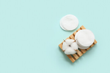 Wooden soap dish with cosmetic pads and cotton flower on color background