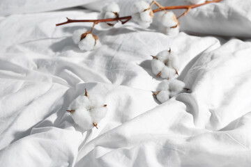 Cotton sprig and flowers on white bed sheets