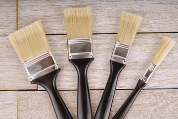 Set of clean paintbrushes with black handles and beige bristles arranged on rustic wooden background.