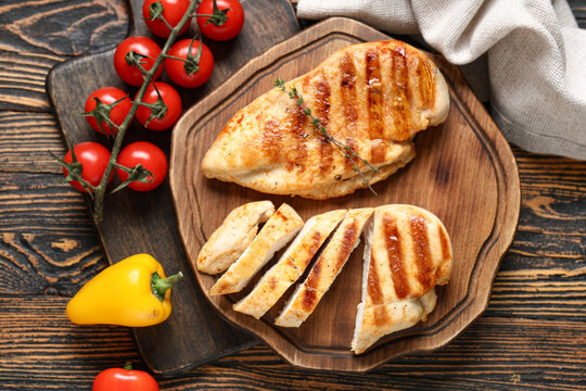 Boards with tasty grilled chicken breast, thyme, tomatoes and bell peppers on wooden background