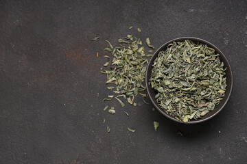 Bowl with dried green tea leaves on black background