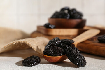 Wooden spoon and bowl with dried prunes on white table