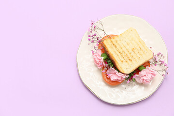 Plate with sandwich and beautiful flowers on lilac background