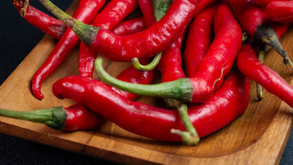Close-up of red chili peppers with fresh green stems on a wooden tray. Suitable for cooking or culinary articles