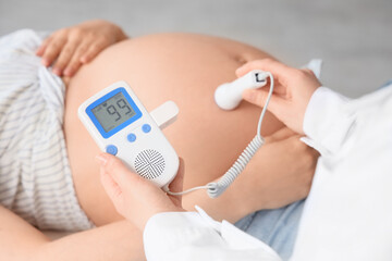 Young pregnant woman and doctor with fetal doppler listening to baby's heartbeat in clinic, closeup
