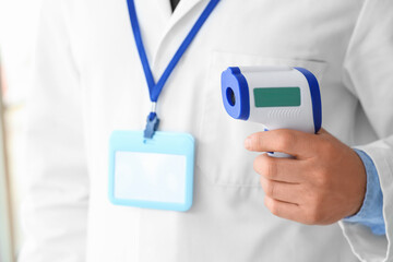Male doctor with infrared thermometer in clinic, closeup