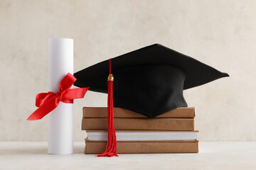 Graduation hat, books and diploma on light background