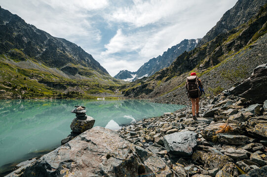 A tourist girl with a backpack walks along the shore of Kuyguk mountain lake in Altai