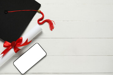 Graduation hat, mobile phone and diploma on white wooden background, top view