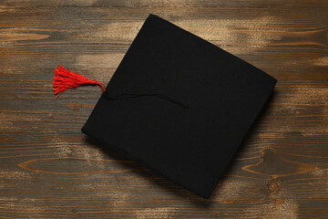 Graduation hat on wooden background, top view