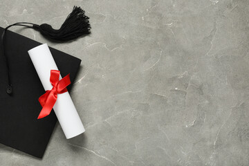 Graduation hat and diploma on grey background, top view