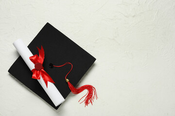Graduation hat and diploma on white background, top view