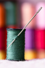 A spool of green thread with a sewing needle through it, colorful spools stacked up in the...