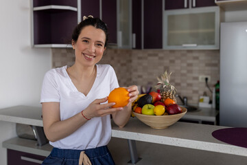 Beautiful active female standing with happy face, enjoying eating fruits, healthy foods for health care wellness to lose weight in house. Diet concept. Fitness and healthy food