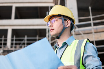 Asian male engineer is looking at the blueprints at the construction site