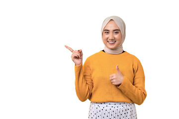 Beautiful cheerful Asian girl wearing hijab pointing finger at empty copy space and giving thumbs...