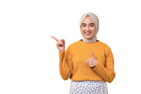 Beautiful cheerful Asian girl wearing hijab pointing finger at empty copy space and giving thumbs up isolated on transparent background