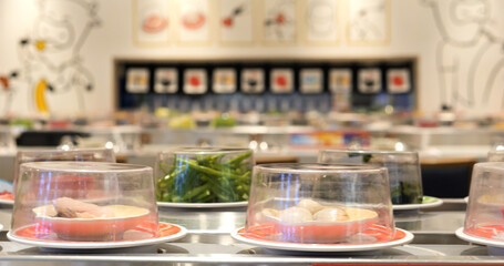 Plates filled with a variety of fresh ingredients moving along a conveyor belt in a modern restaurant, awaiting selection by customers for an enjoyable cooking experience