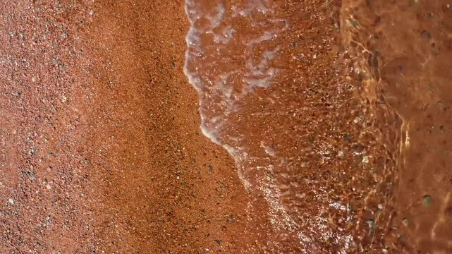 This closeup footage shows the texture of sandy shores and the waves gently rolling in at Assyk Kul Lake, Kyrgyzstan, capturing the tranquil beauty of the lake.