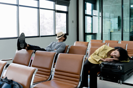 Tired travelers sleeping in airport waiting area, man napping on chairs with hat over face and woman resting on suitcase, exhausted during flight layover