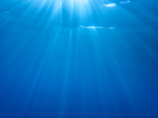 Dark blue ocean surface seen from underwater. Abstract waves underwater and rays of sunlight shining through, Sun light rays undersea deep, Underwater background with sea bottom, Mediterranean sea.