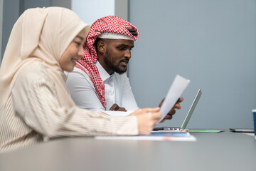 Female muslim businesswoman in hijab discussing business strategy with arab middle eastern man in modern office work on laptop, professional teamwork, communication, collaboration, diversity concept