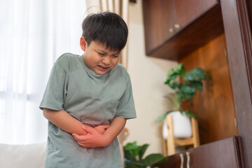 Portrait of sick unhappy little child asian boy touching belly stomach with suffering from stomach...