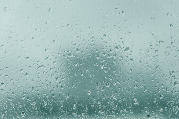 6月梅雨　窓ガラスについた雨粒の水滴と雨垂れ　街の背景　風に流されて降る雨と都市景観