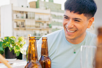 Young man smiles happily, an afternoon of informal gathering outdoors on a terrace, with beers