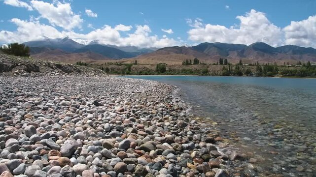 Assyk Kul Lake in Kyrgyzstan features a rocky pebble shore with clear water, offering a tranquil and beautiful setting perfect for nature photography and exploration.