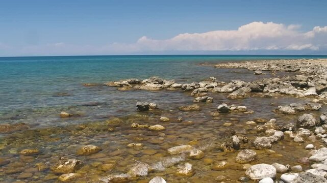 Footage shows the stunning rocky beach and clear waters of Assyk Kul Lake in Kyrgyzstan, offering a peaceful and scenic environment with surrounding natural beauty.