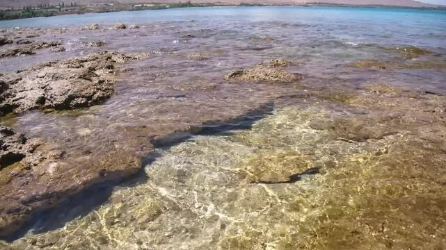 Footage showcases the rocky beach bed of Assyk Kul Lake with stunning, clear turquoise waters, offering a serene and picturesque landscape perfect for nature lovers.