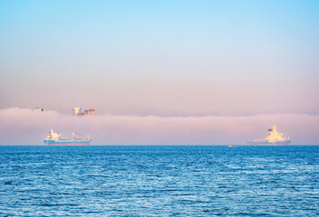 Ships navigating through foggy waters during early morning near the coast