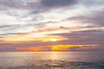 Beautiful twilight sky with dramatic orange clouds reflecting over serene sea at sunset.